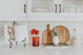 Kitchen scene with cookbook holder, utensils, cutting boards, cheese boards, and cabinets of dishes for home organization hacks