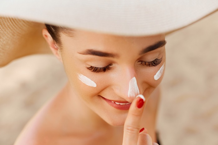 Beautiful happy cute woman applying suntan cream to her nose