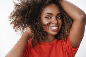 carefree relaxed and tender african-american female model in red t-shirt playing with curly hair