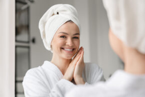 Girl getting ready with towel on wet hair smiling into mirror
