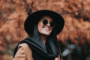 Girl smiling wearing sunglasses, scarf, and fedora hat
